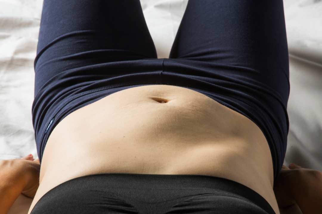 Žena ležící na zádech zvedá nohy a kontroluje diastázu břišních svalů
