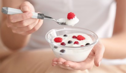 Žena jí lžičkou bílý jogurt s ovoce, aby snížila svůj krevní tlak
