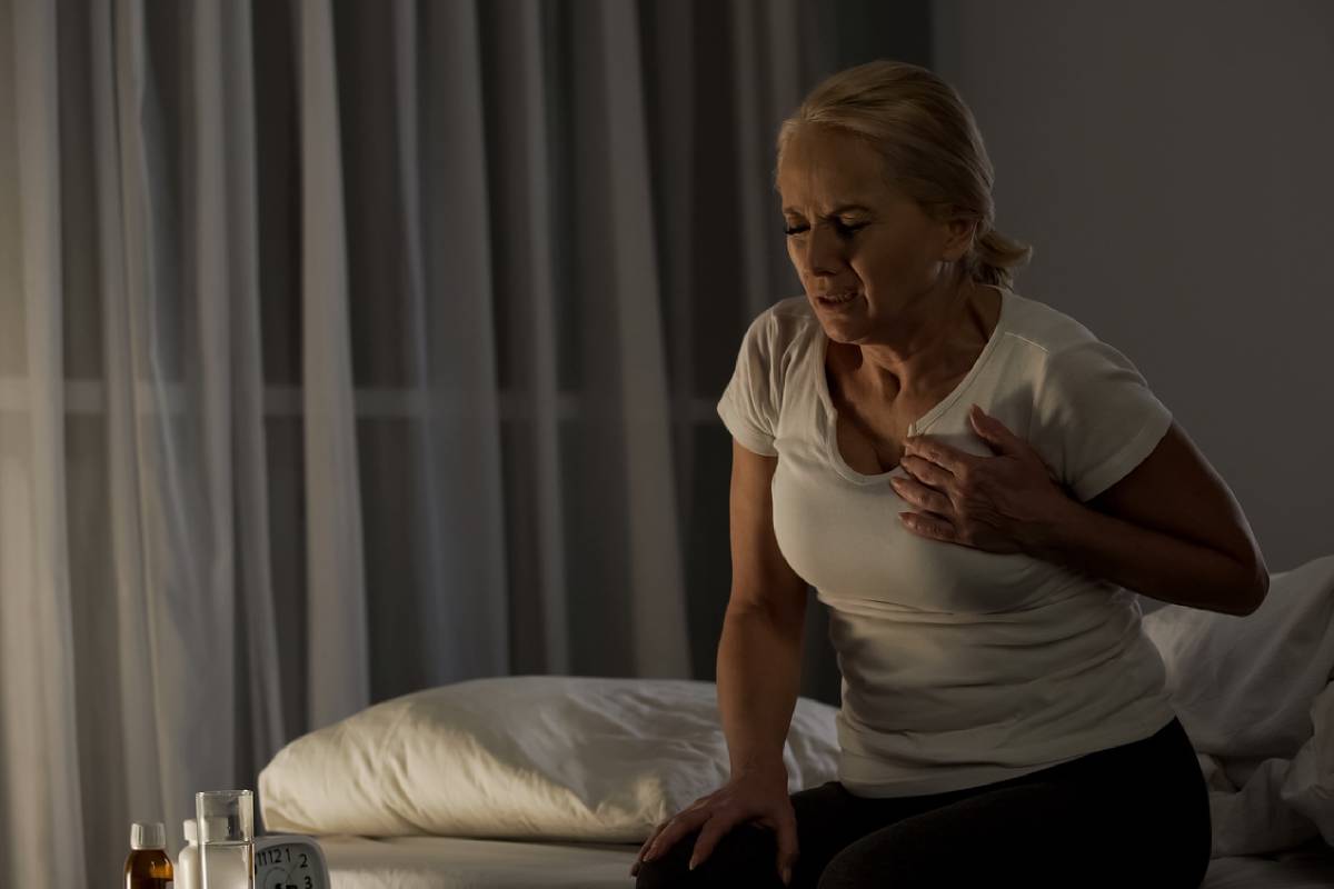 Žena sedící na posteli v noci s bolestí na hrudi