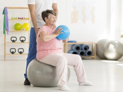 starší žena sedí na gymnastickém míči a drží menší míč při posilování pánevního dna