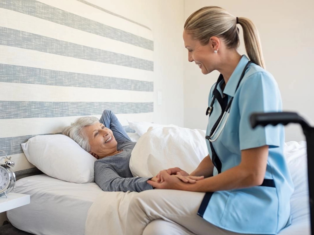 sestra drží seniorku za ruku na lůžku