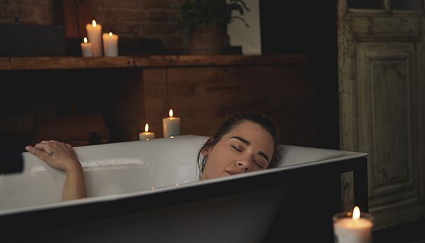 Žena relaxuje ve své vaně se zapálenými svíčkami kolem sebe